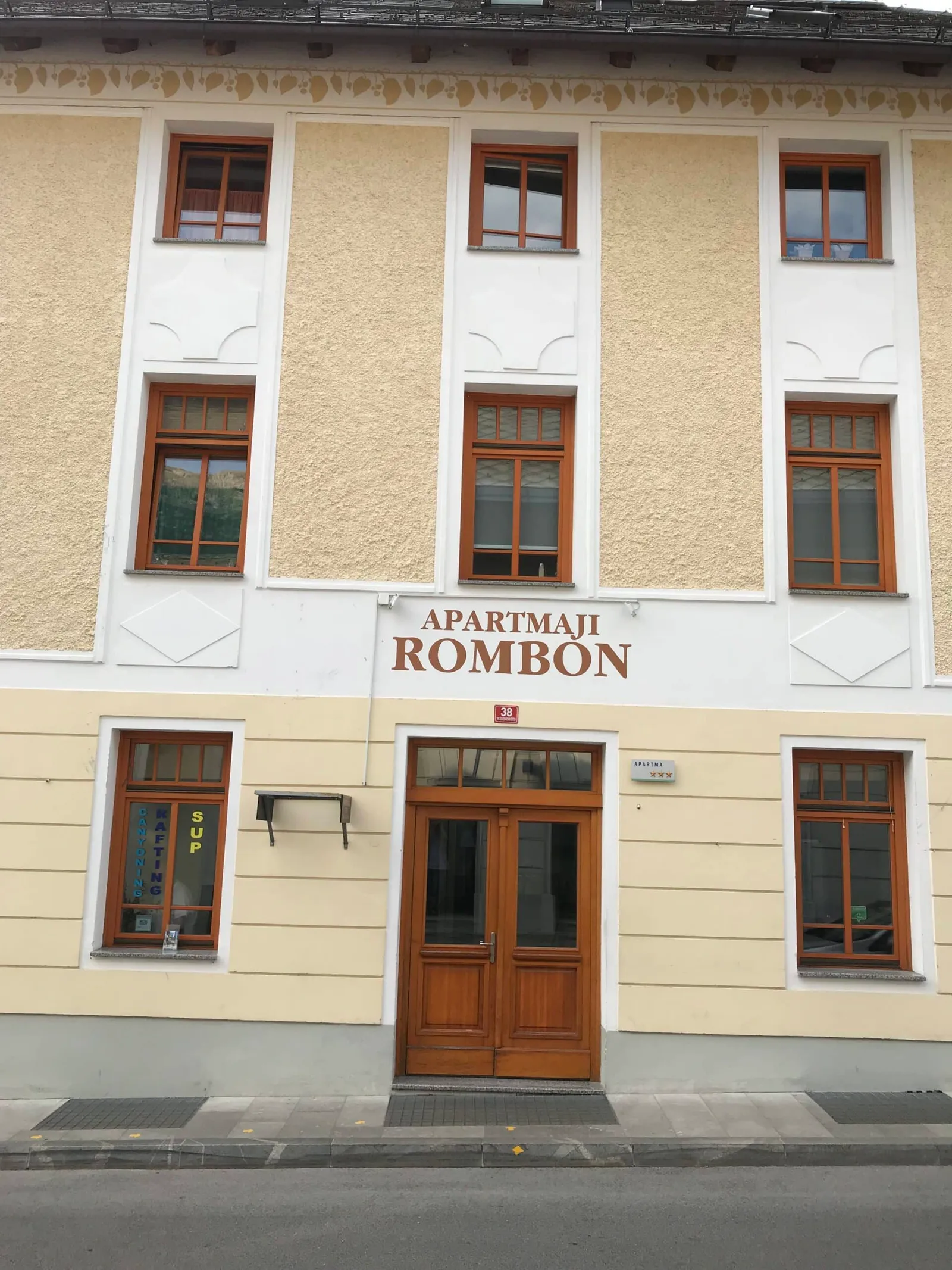 Pročelje hiše z napisom Apartmaji Rombon in lesenimi vrati
